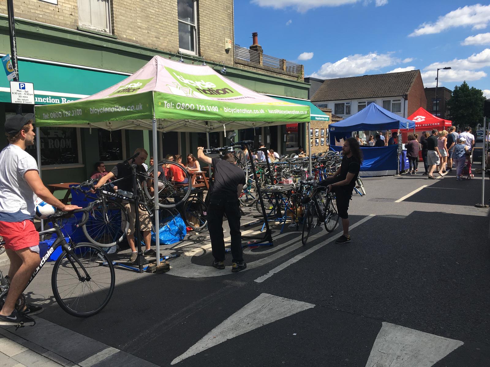 Outdoor market scene with people, bicycles, and colorful tents on a sunny day.