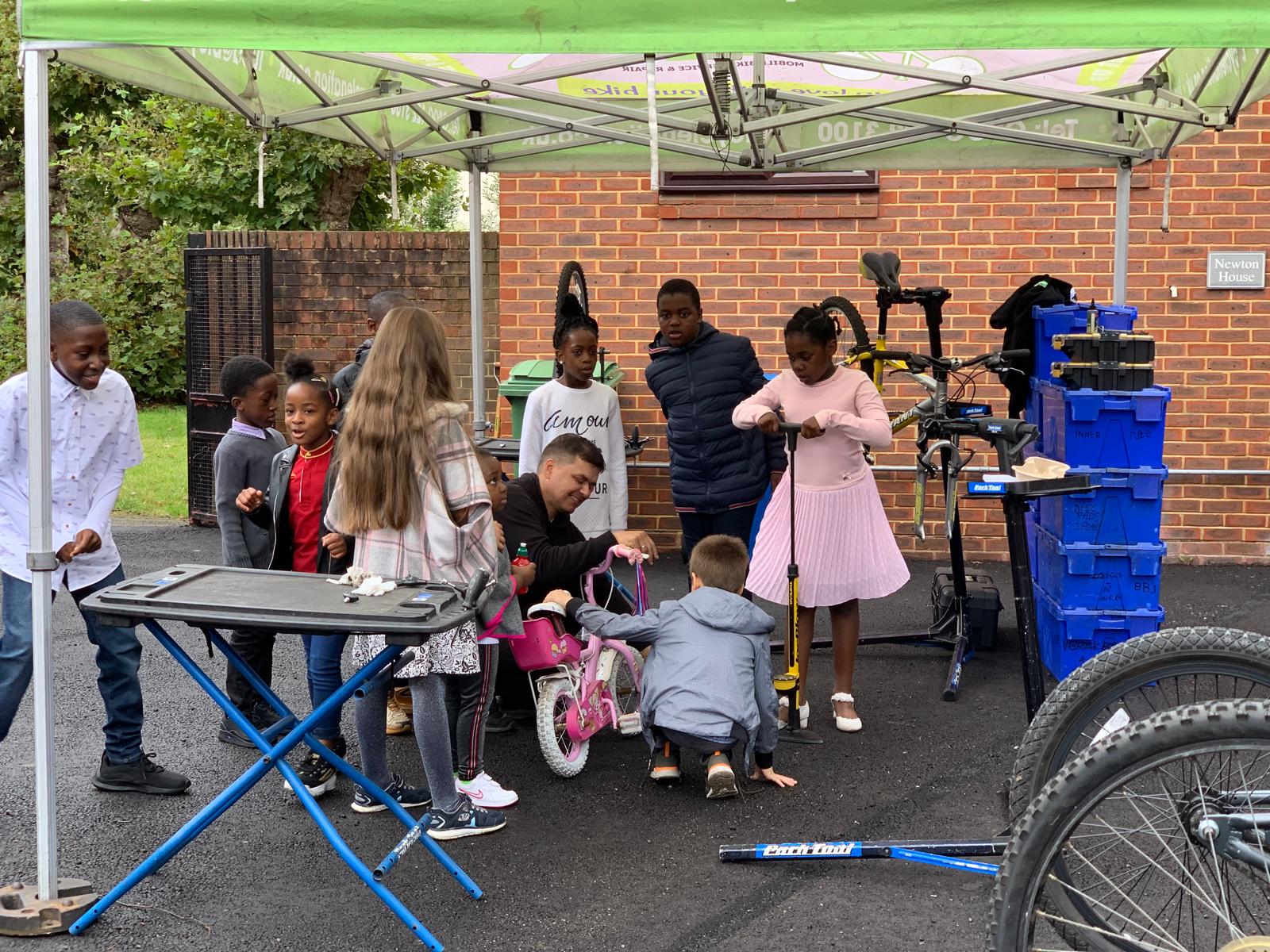 Children playing with bicycles under a green canopy in an outdoor setting.