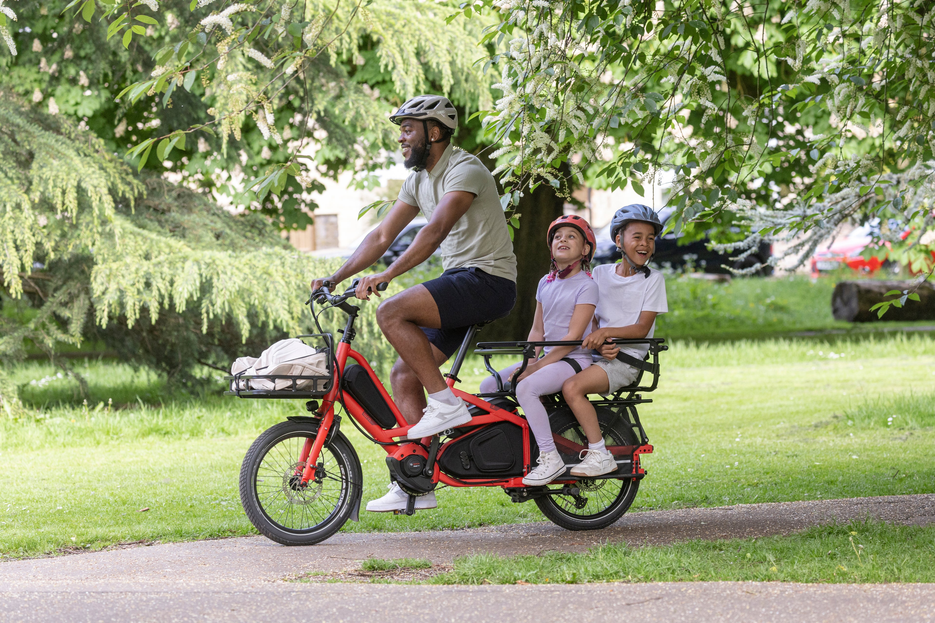Man riding a red electric bike with two children in a park