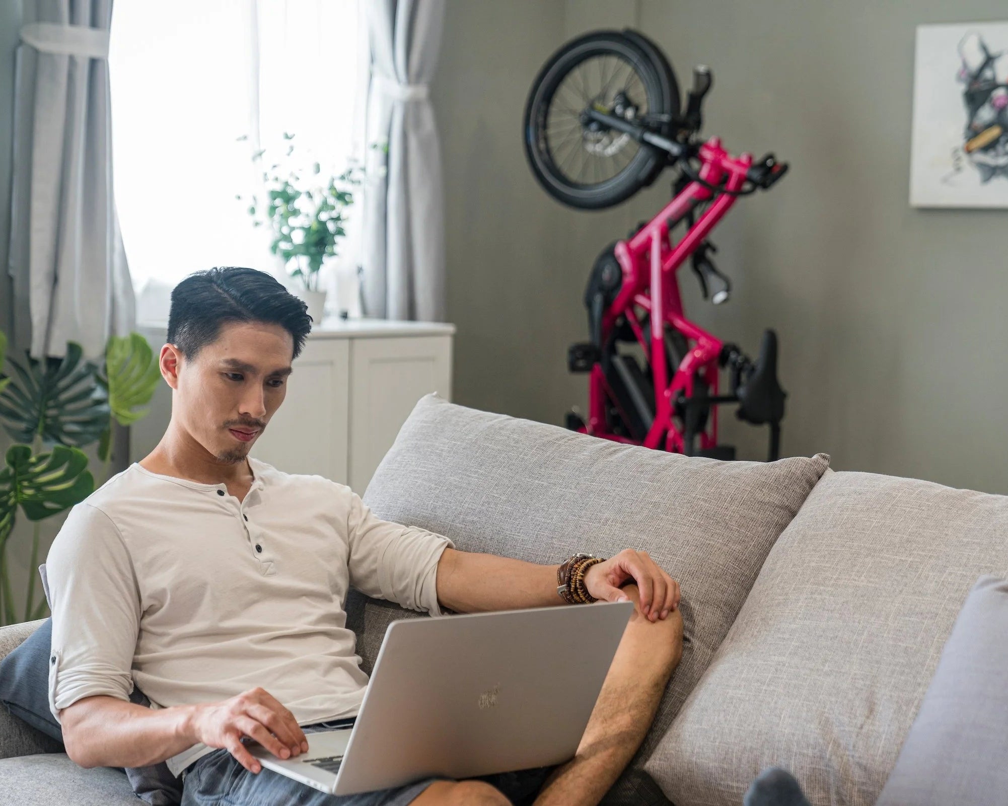 Man using a laptop on a couch in a living room with a bicycle in the background
