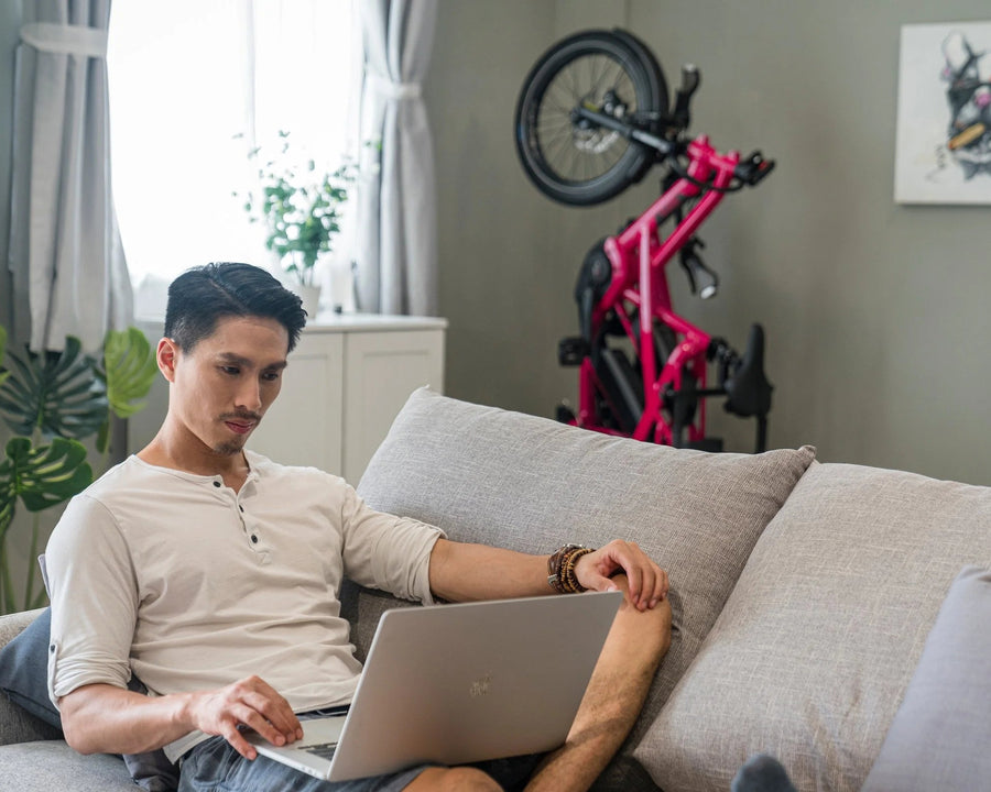 Man using a laptop on a couch in a living room with a bicycle in the background
