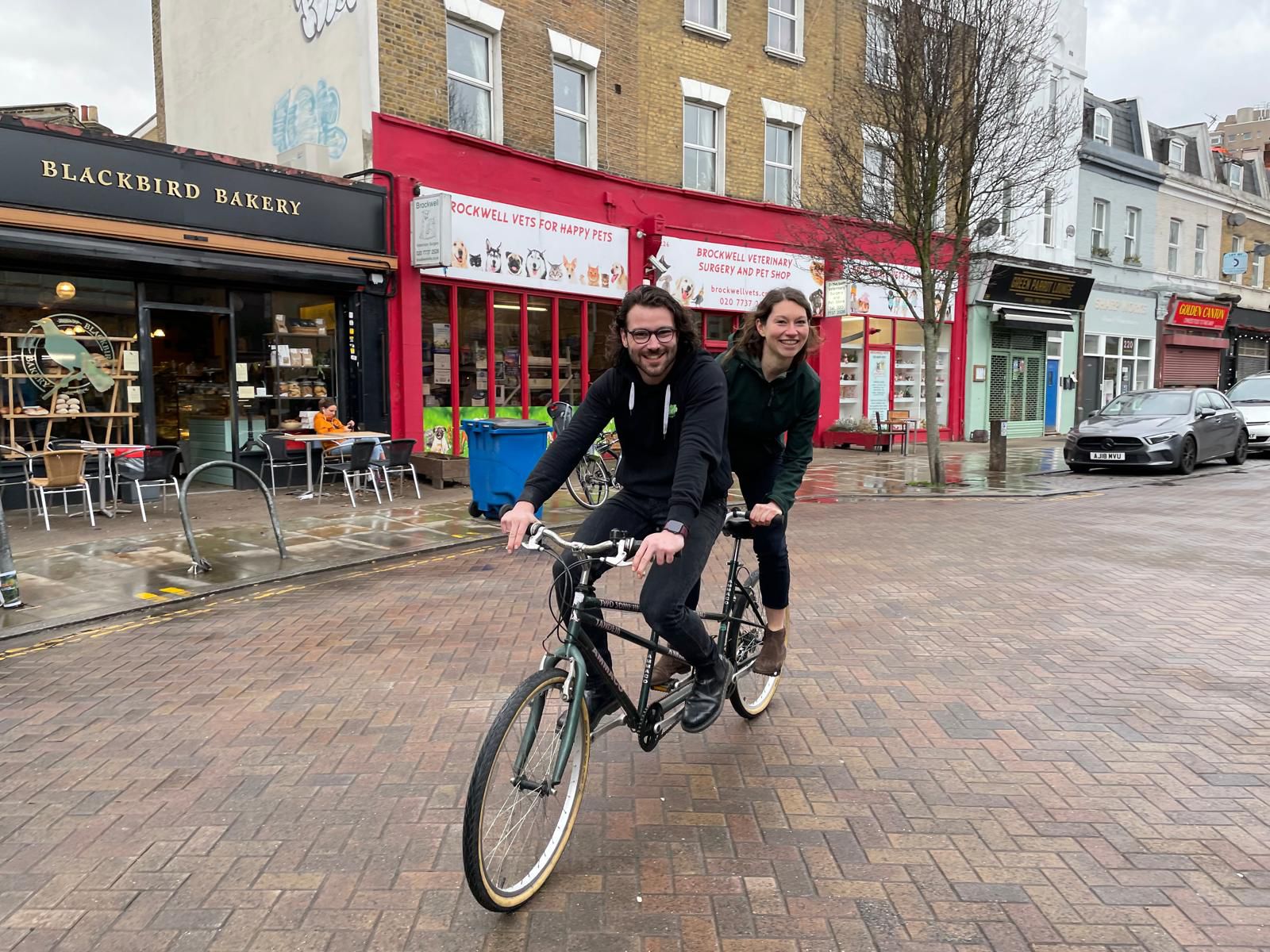 A man and a woman riding a tandem bicycle in London. 