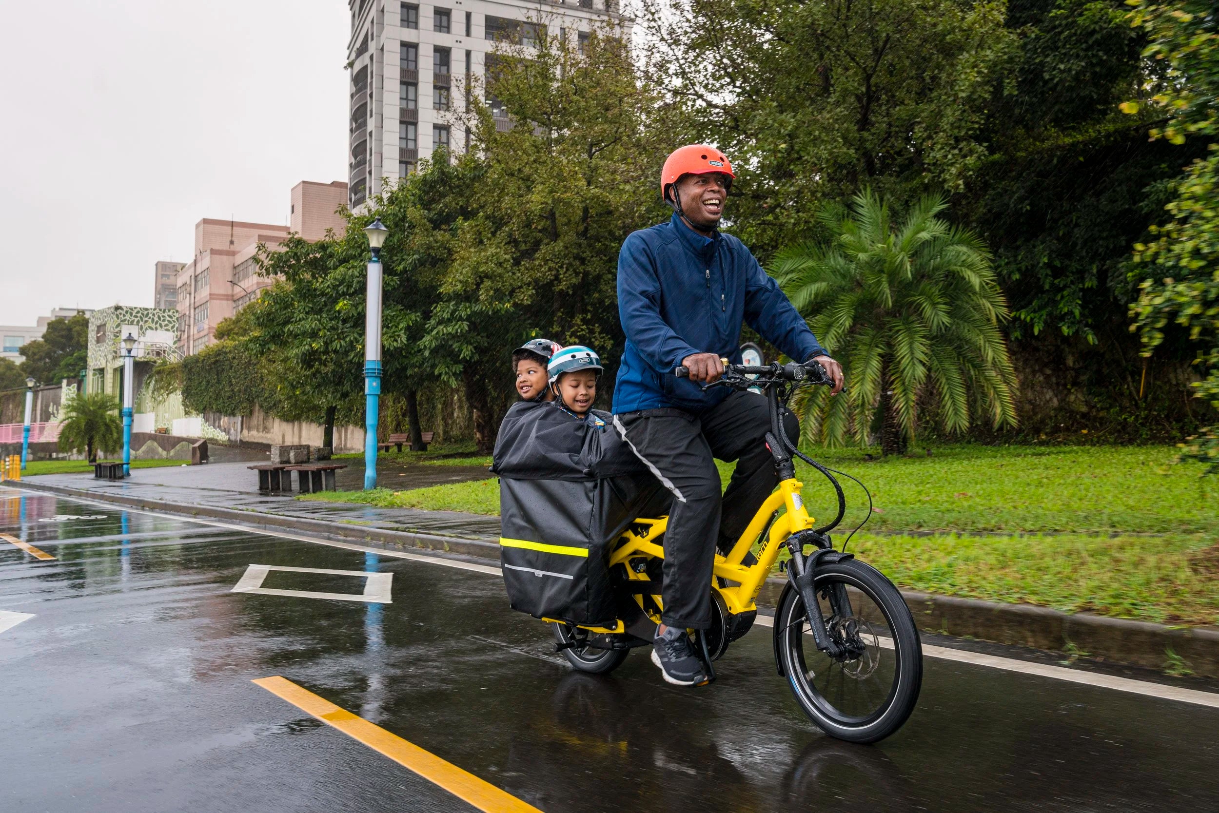 Man and two children riding a yellow electric bike on a rainy day.