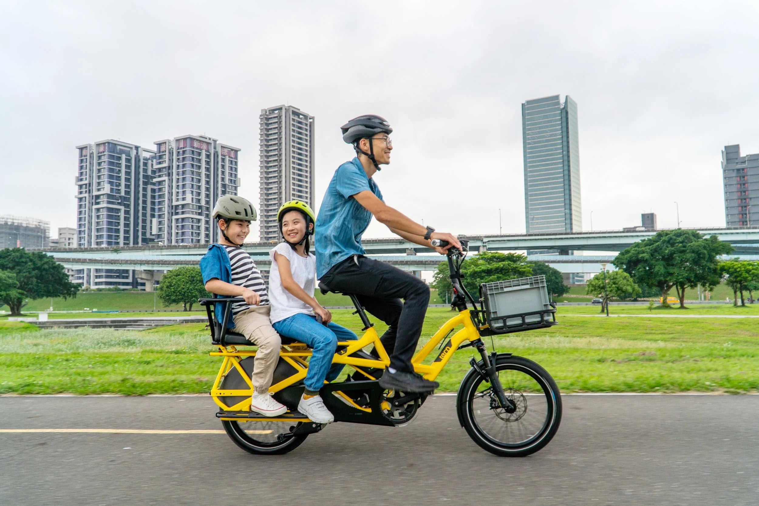 Family riding a yellow electric bike in an urban park setting