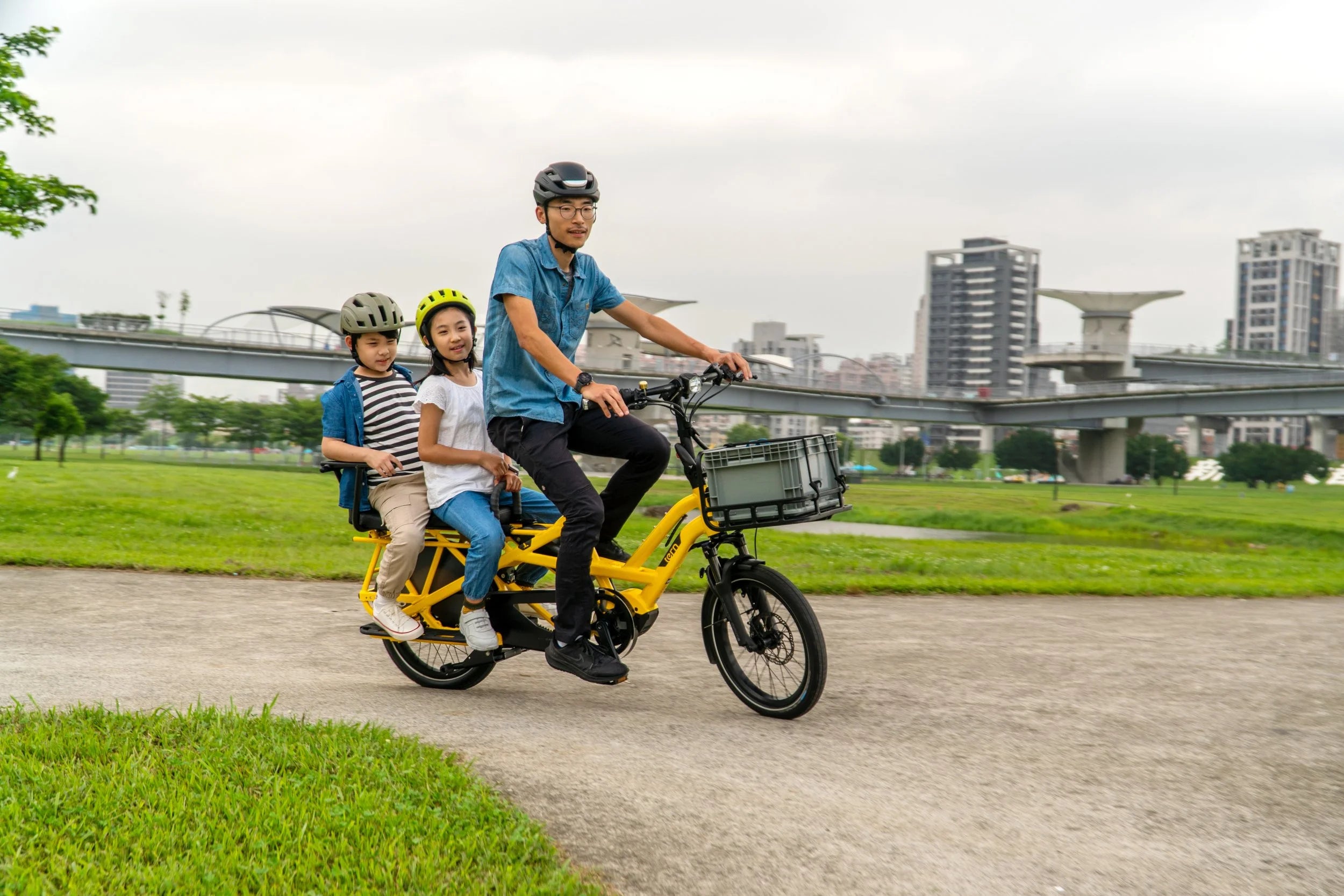 Family riding a yellow electric bike in an urban park setting