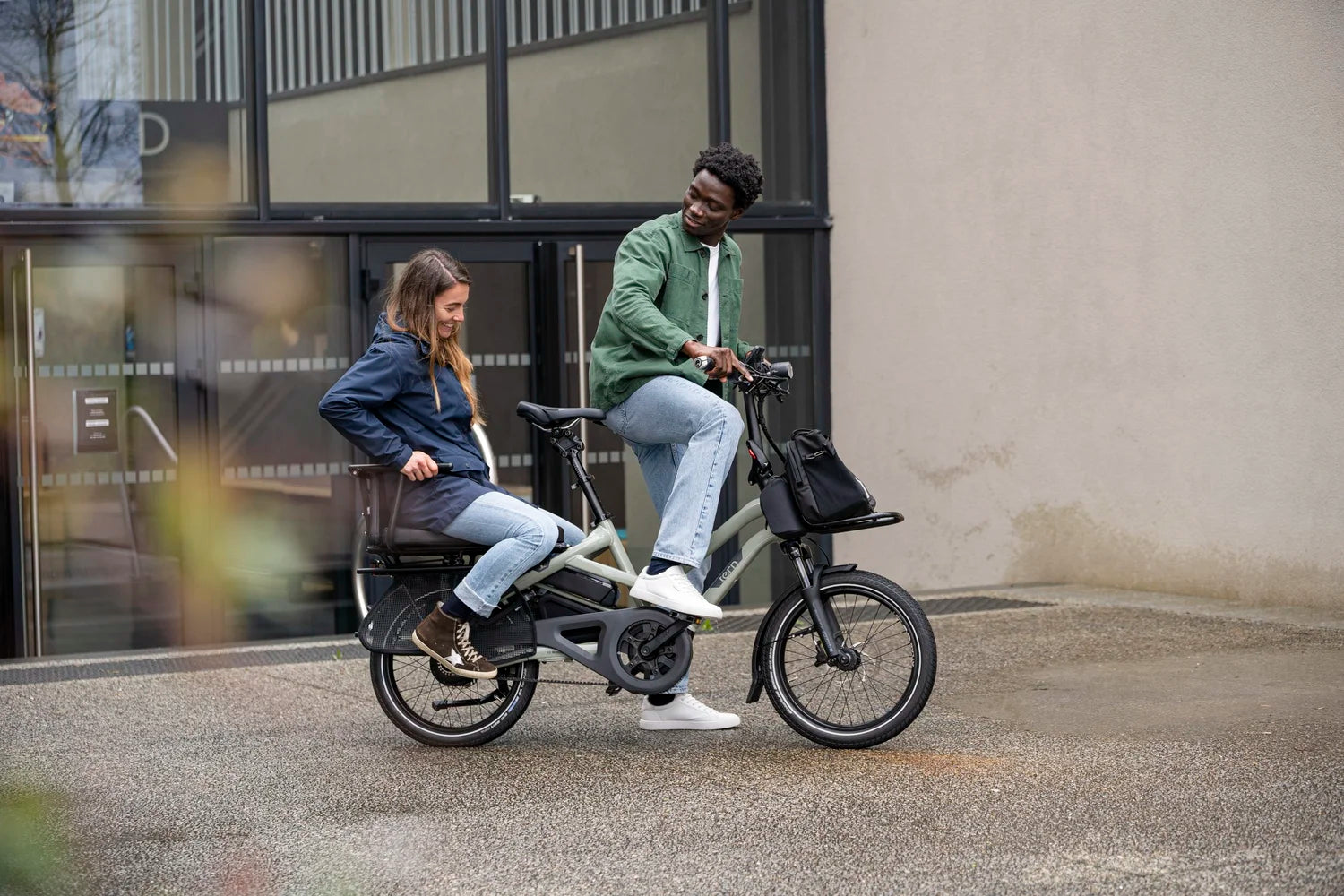 Two people riding a Tern electric bike on a city street.