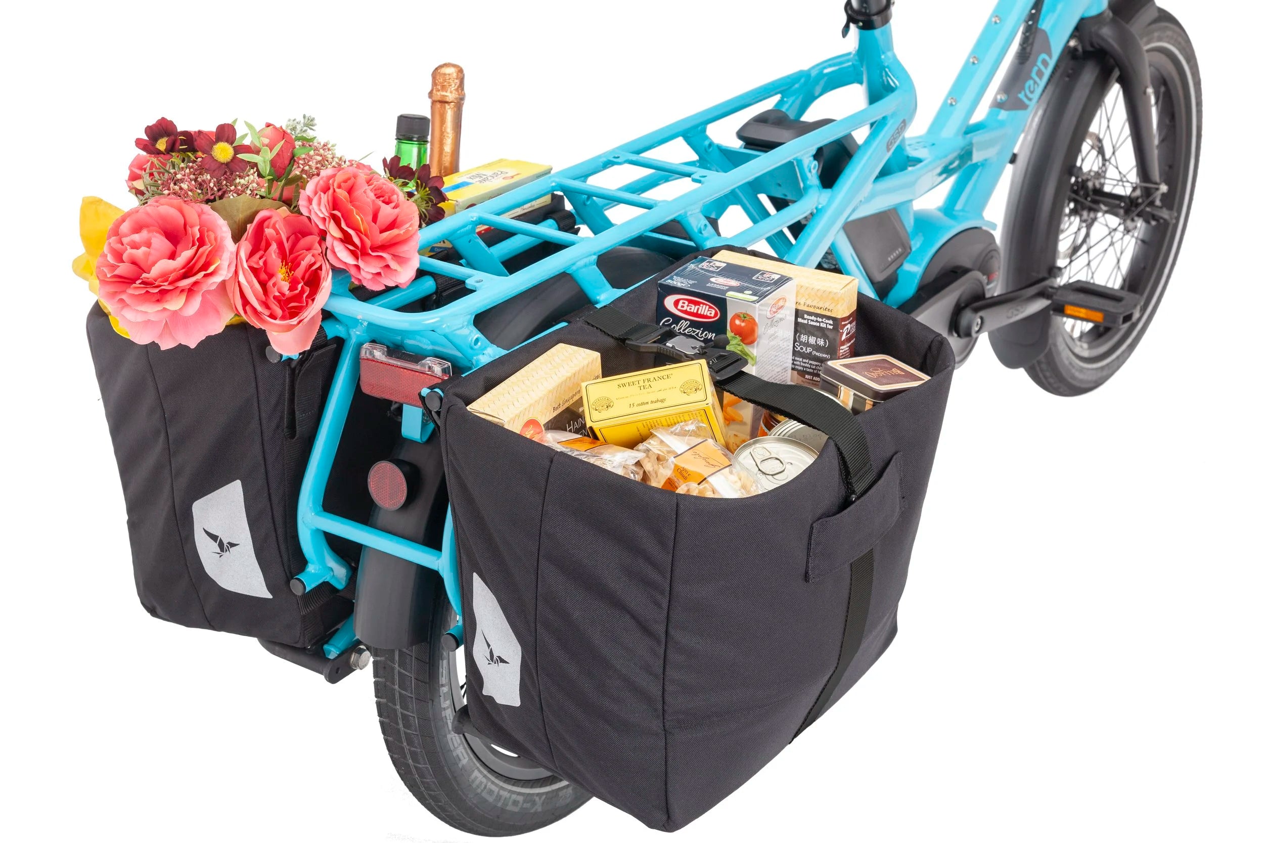Blue cargo electric bicycle with black bags containing groceries and flowers on a white background