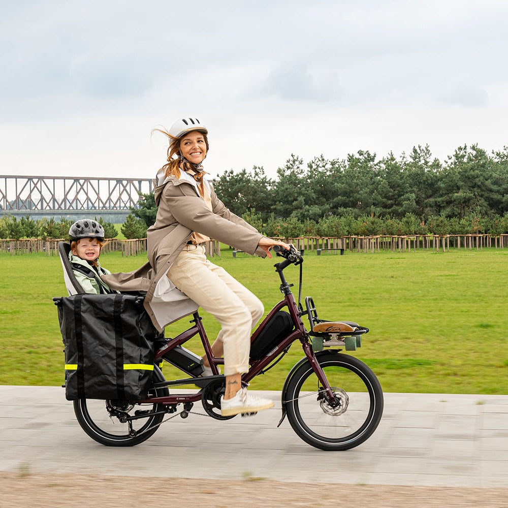 Woman riding a cargo bike with a child in a park-like setting