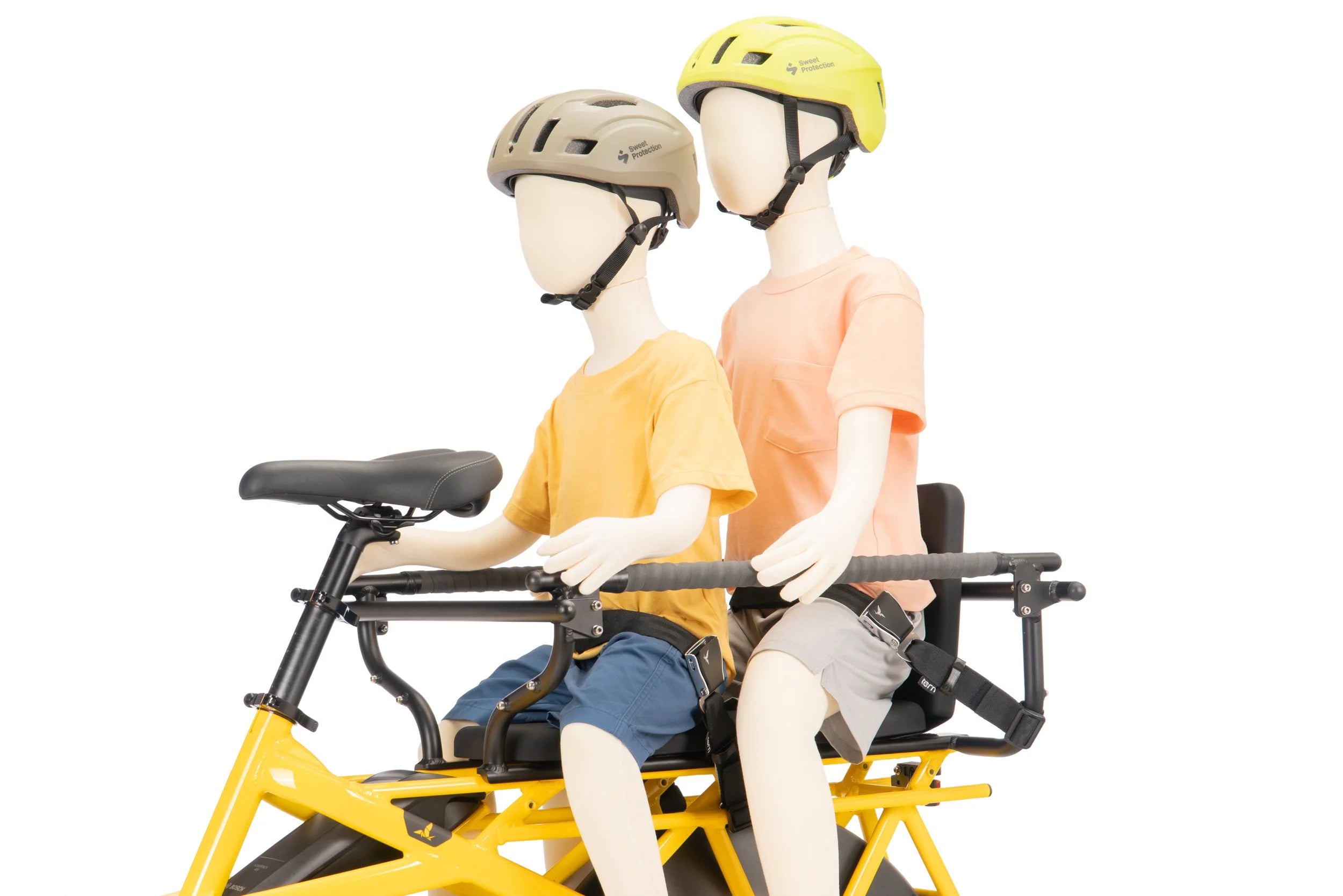 Two mannequins wearing helmets sitting on a yellow bicycle child seat against a white background