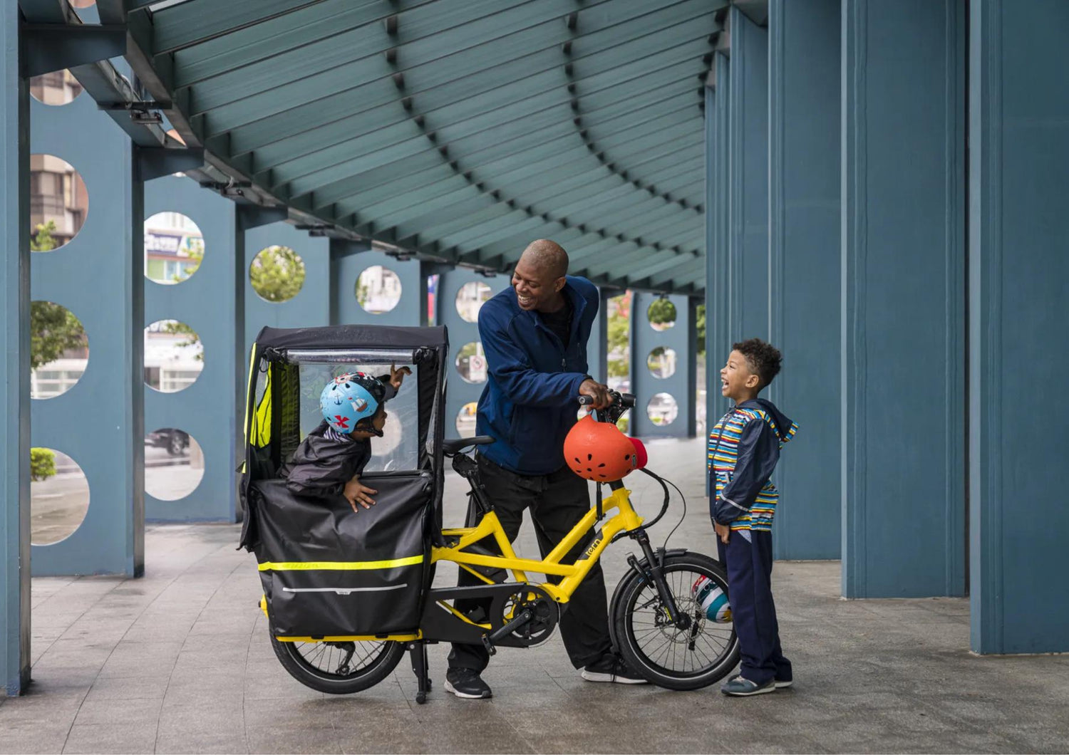 Man with two children using a Tern cargo bike in an urban setting