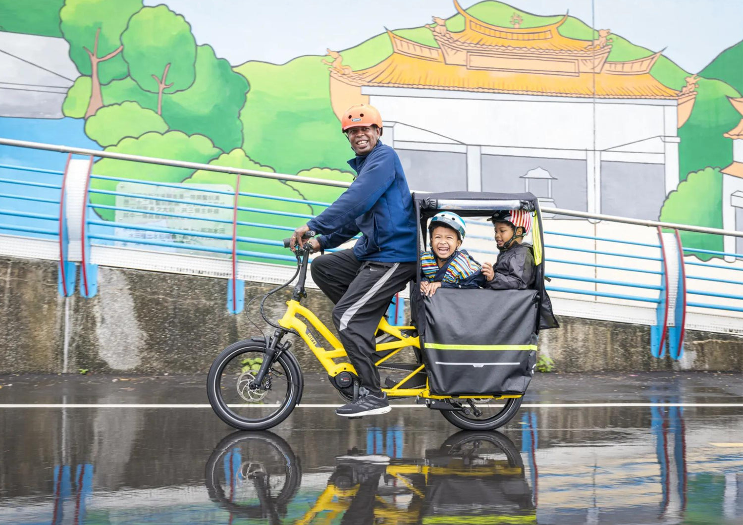 A person riding a yellow Tern cargo bike with two kids in the back carrier.