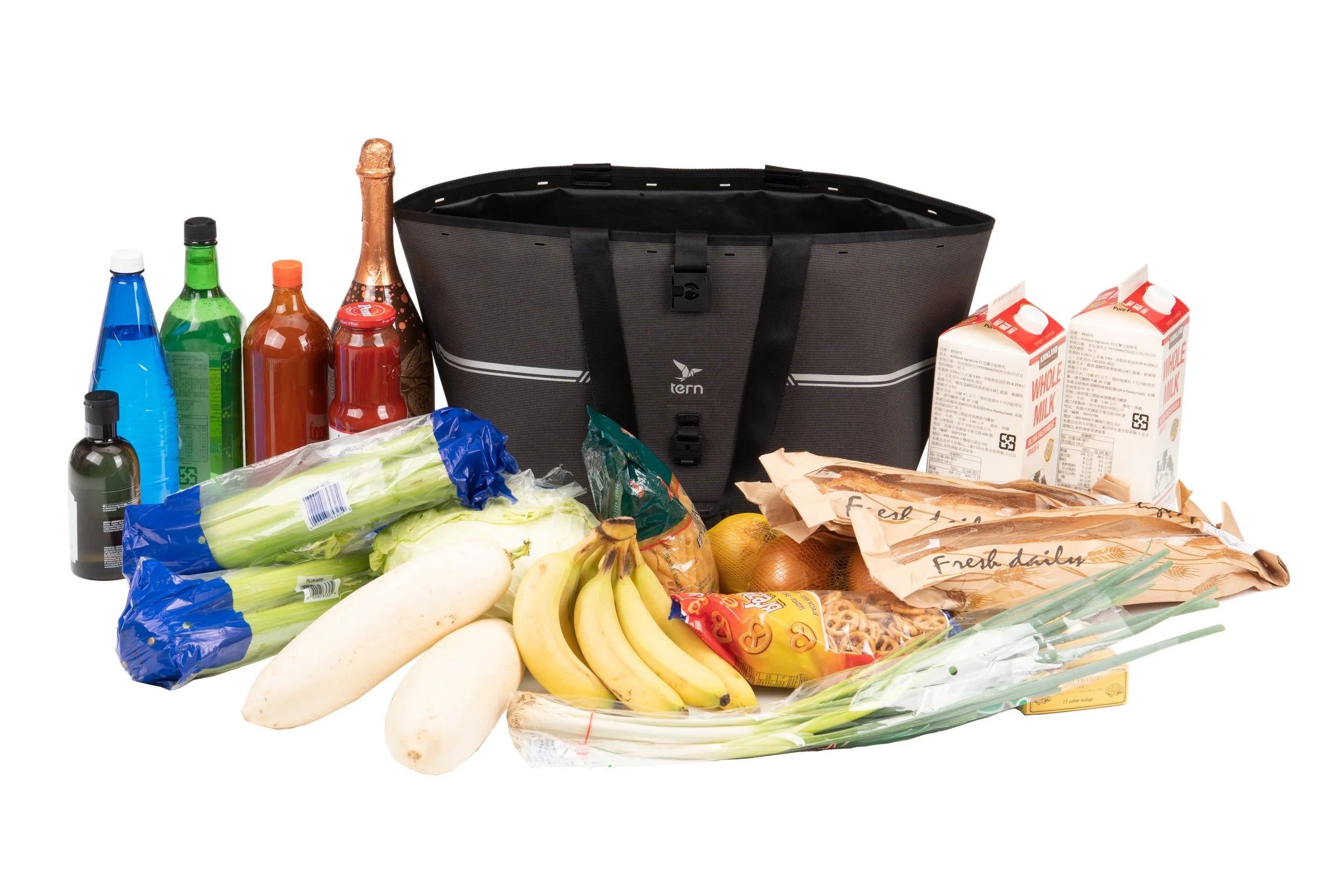 Black bicycle pannier surrounded by groceries including bananas, onions, and bottles on a white background