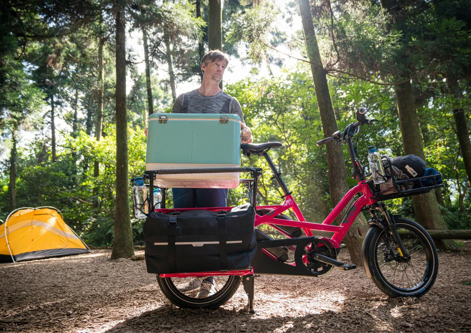 Person with a pink Tern cargo bike in a forest setting, holding a green suitcase.
