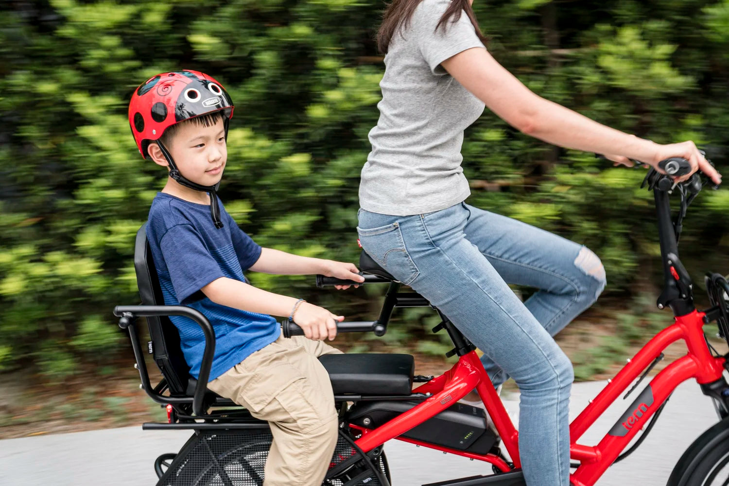 Woman and child riding a red electric bike with a child seat in a park.