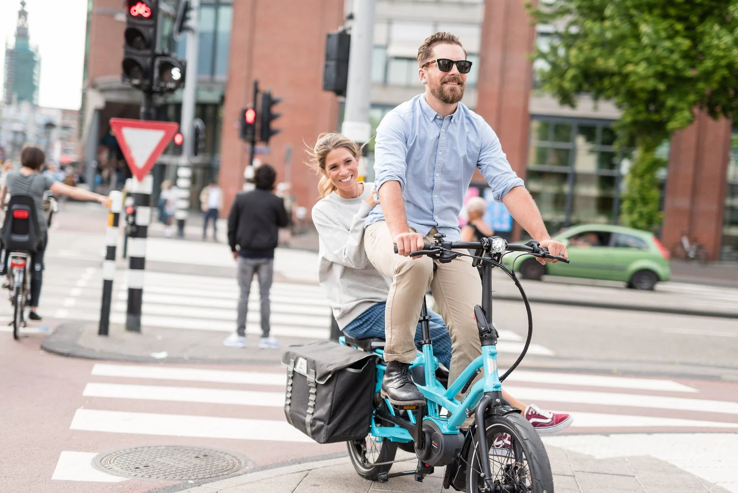 Man and woman riding a teal electric bike on a city street.