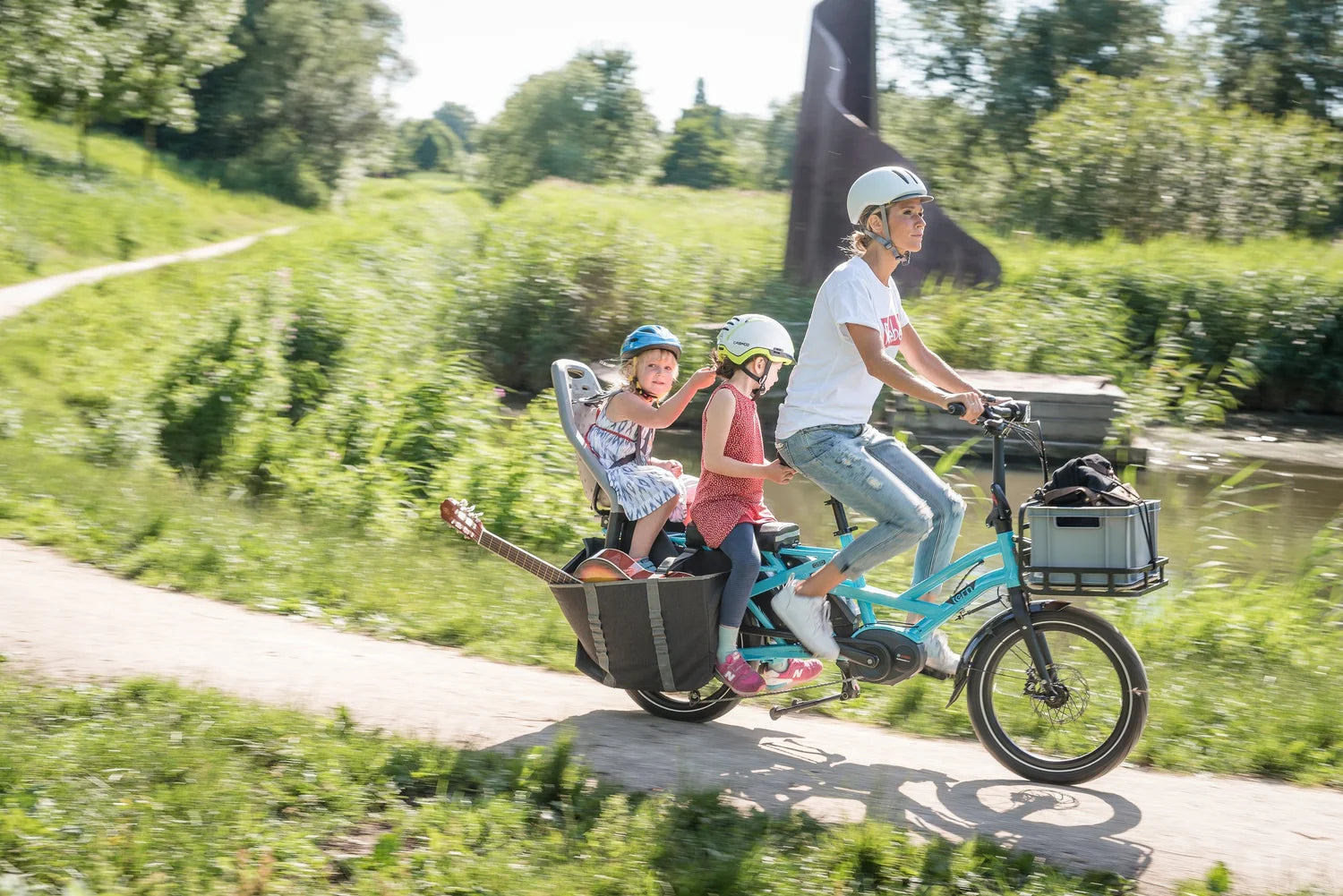 Person riding a cargo bike with children in a trailer on a sunny day.