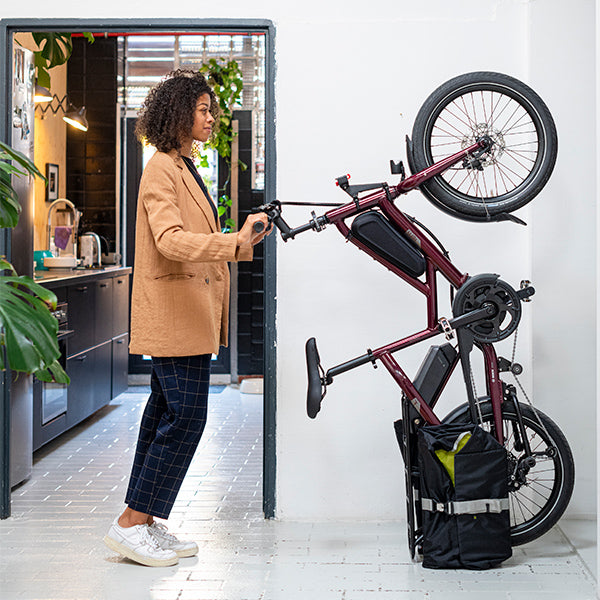 A woman with a purple cargo bike in an upright storage position.