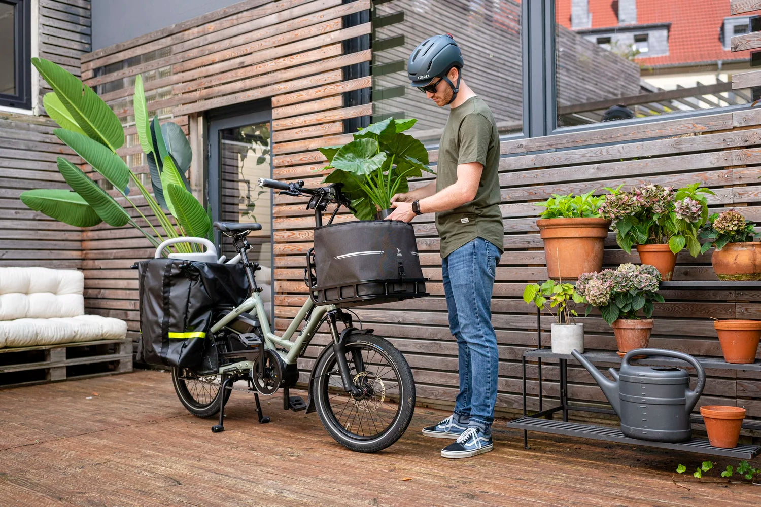 Person with a helmet interacting with an electric bike on a wooden deck with plants and furniture.
