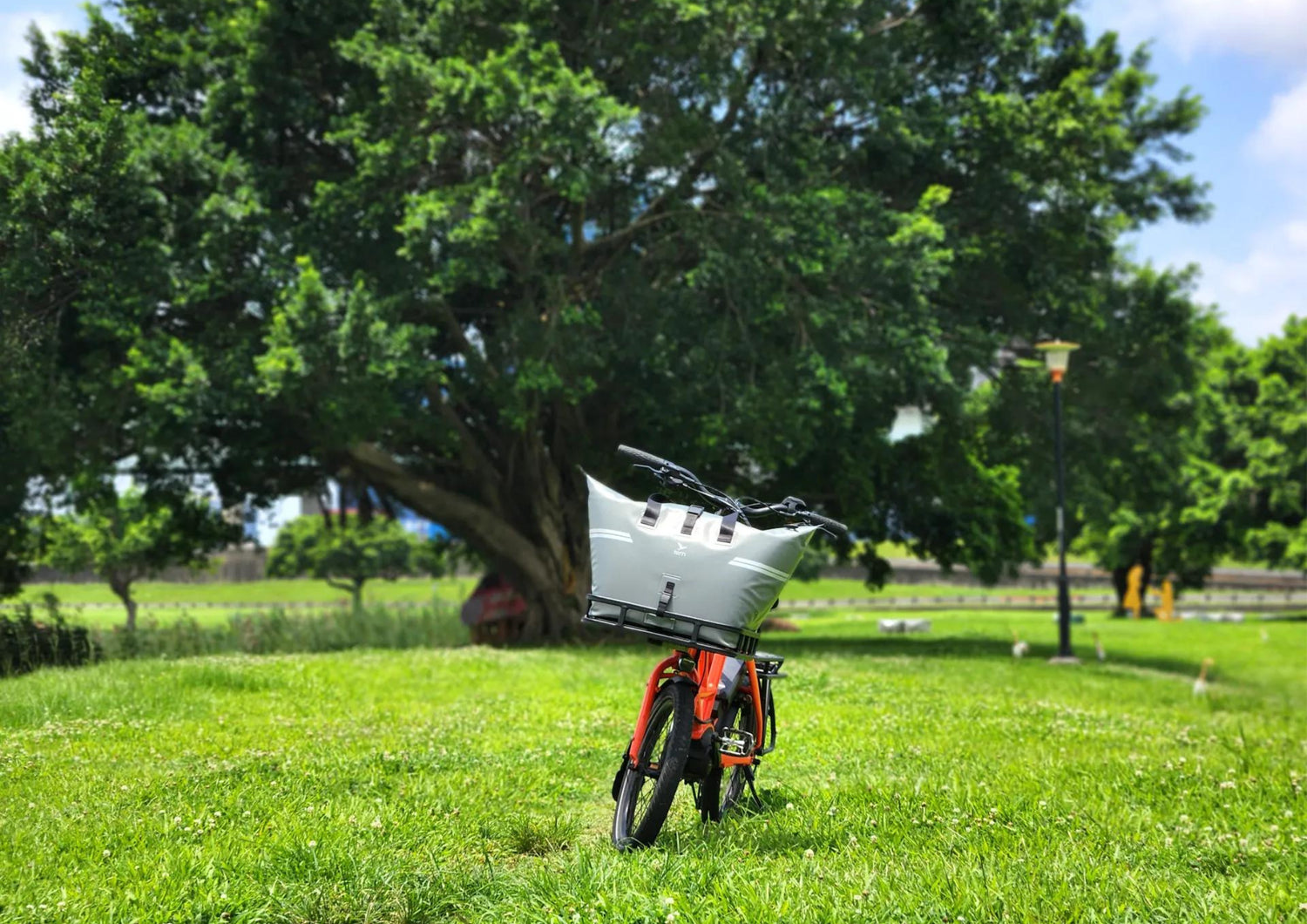 Small red cargo bike with a pannier on its front rack on a grassy area with trees in the background