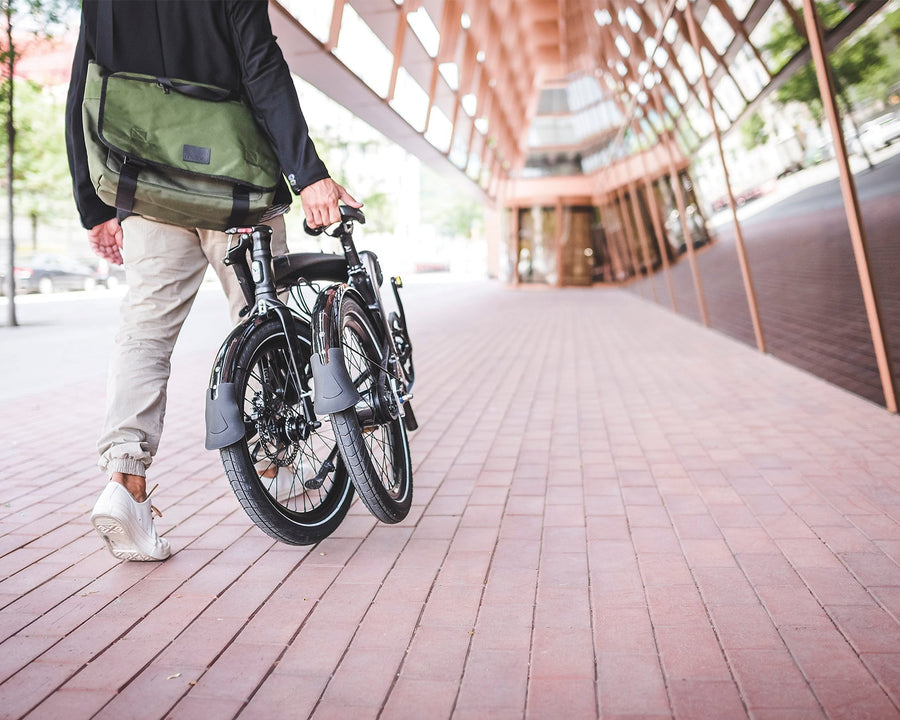 A person walking with a folded Tern Verge bicycle in a city setting