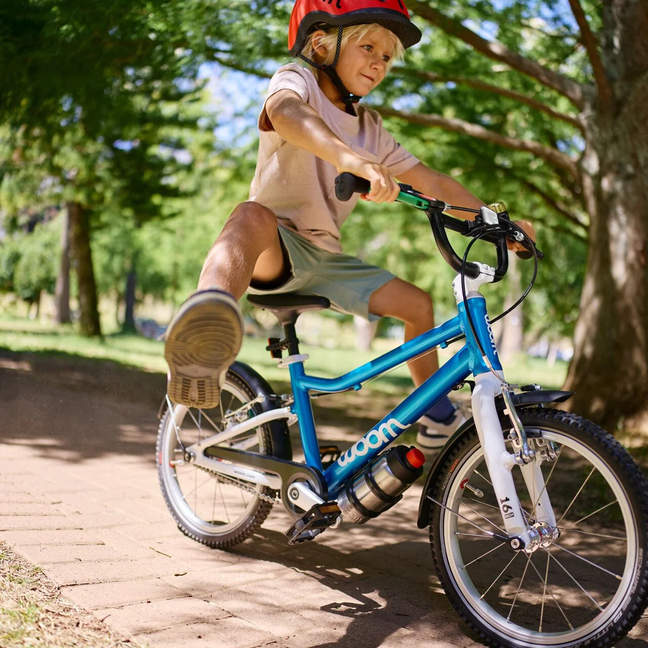 Child riding a Woom blue bicycle on a paved path in a park