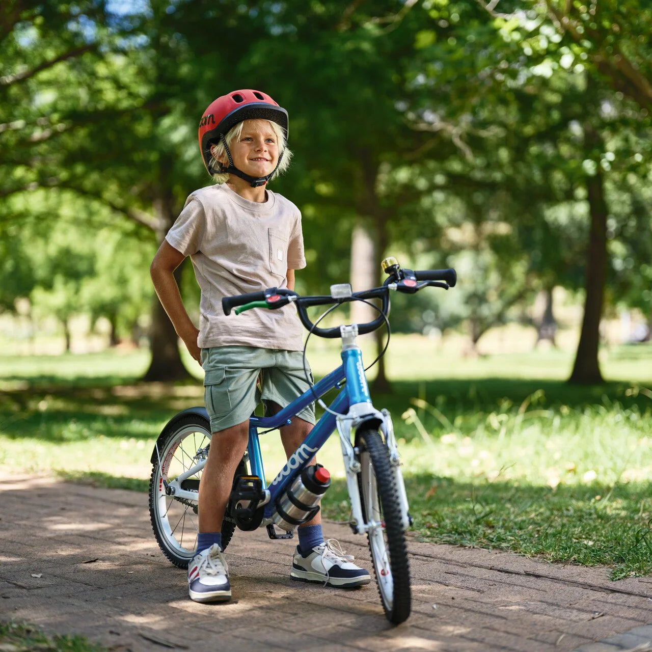 Child standing next to a blue bicycle wearing a helmet in a park setting