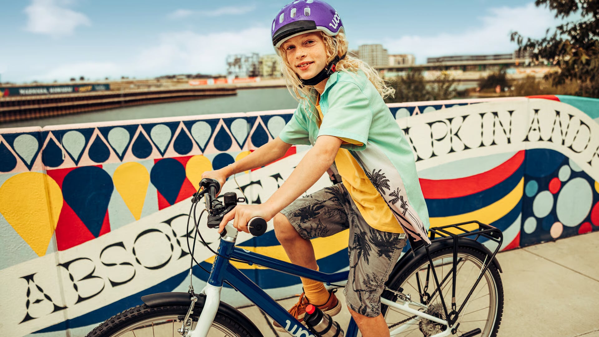 Child on a Woom bicycle in front of a colourful mural with text