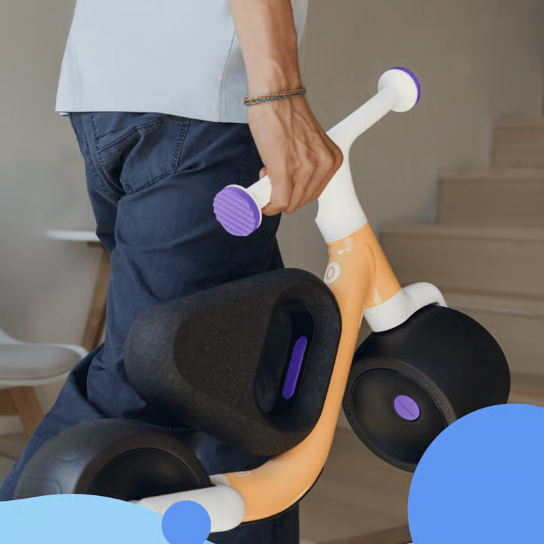 Person holding a children's tricycle with purple accents in a home setting
