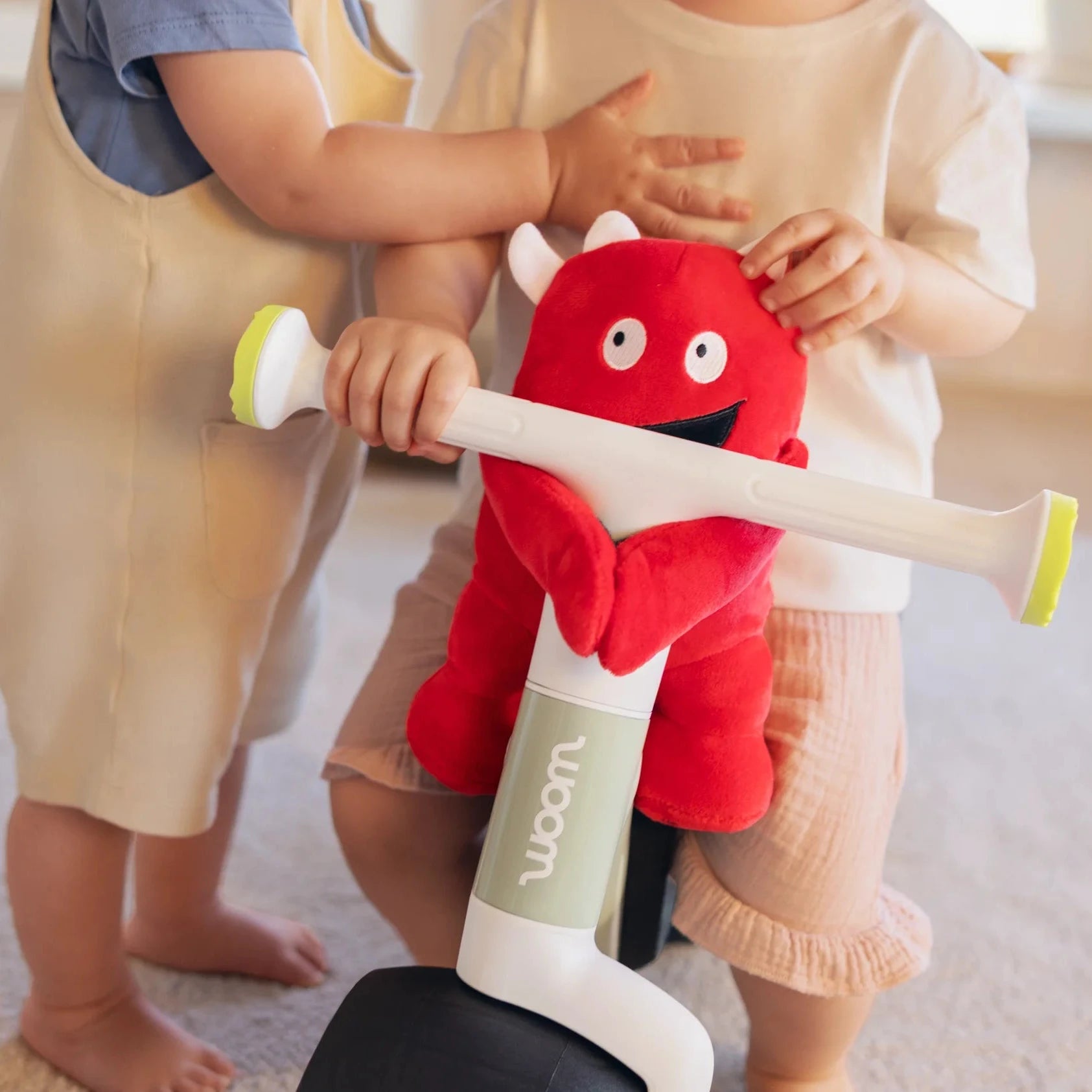 Two children holding a red plush toy with a white handle in a room.