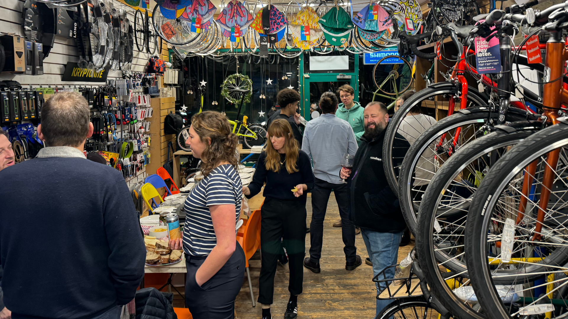 People shopping in a bicycle shop with various bicycles and parts displayed.