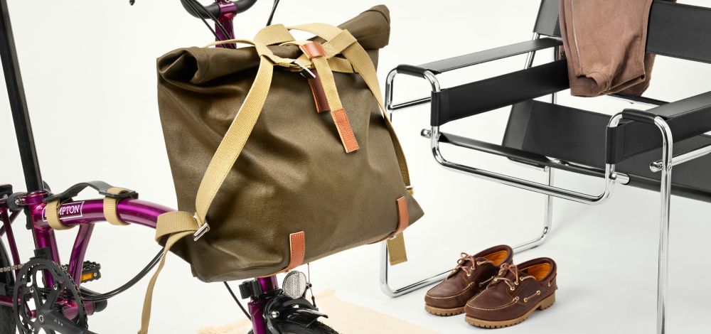 Brown leather bag on a bicycle next to a chair and shoes on a white background