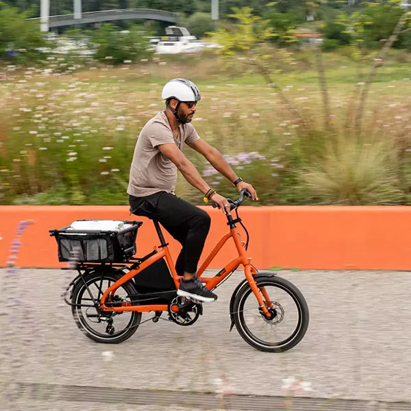 Man riding an orange electric bike on a path with greenery in the background