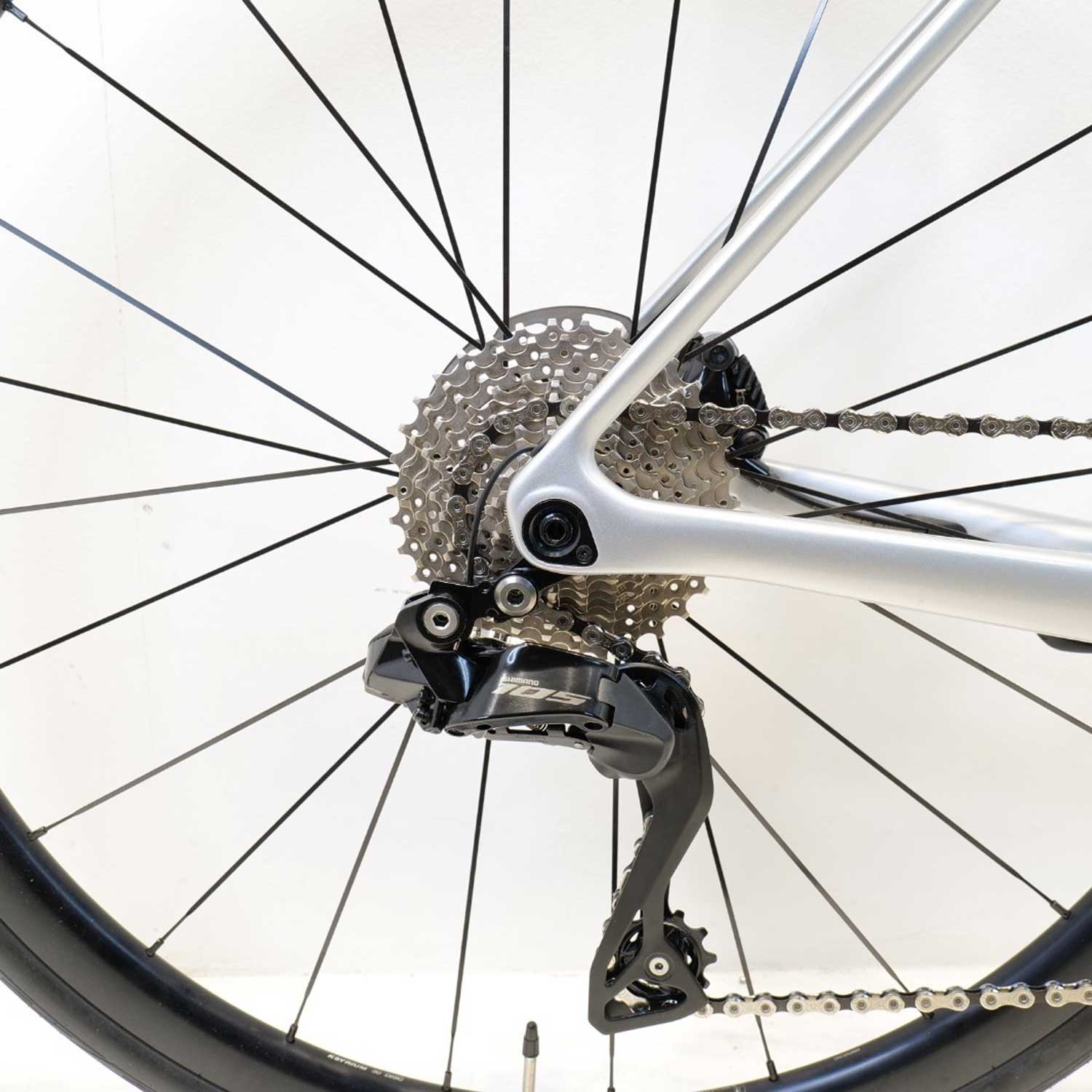 Close up of a bicycle cassette and derailleur with a black wheel and a silver bike frame on a white background.