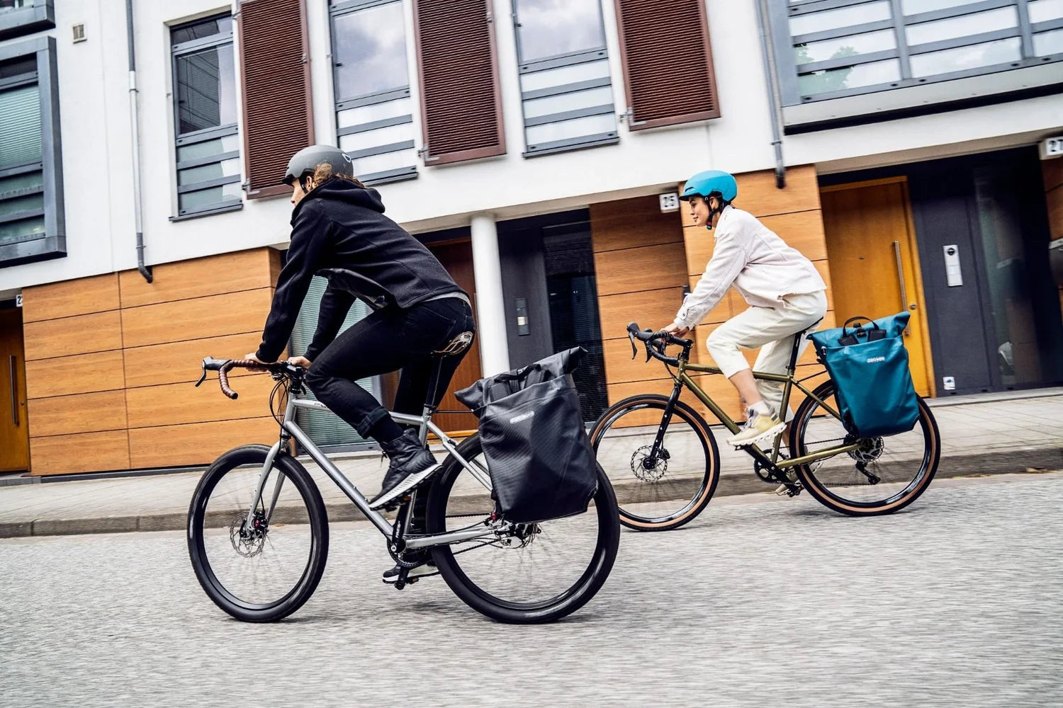 Two people riding bicycles with bags on a street in an urban setting