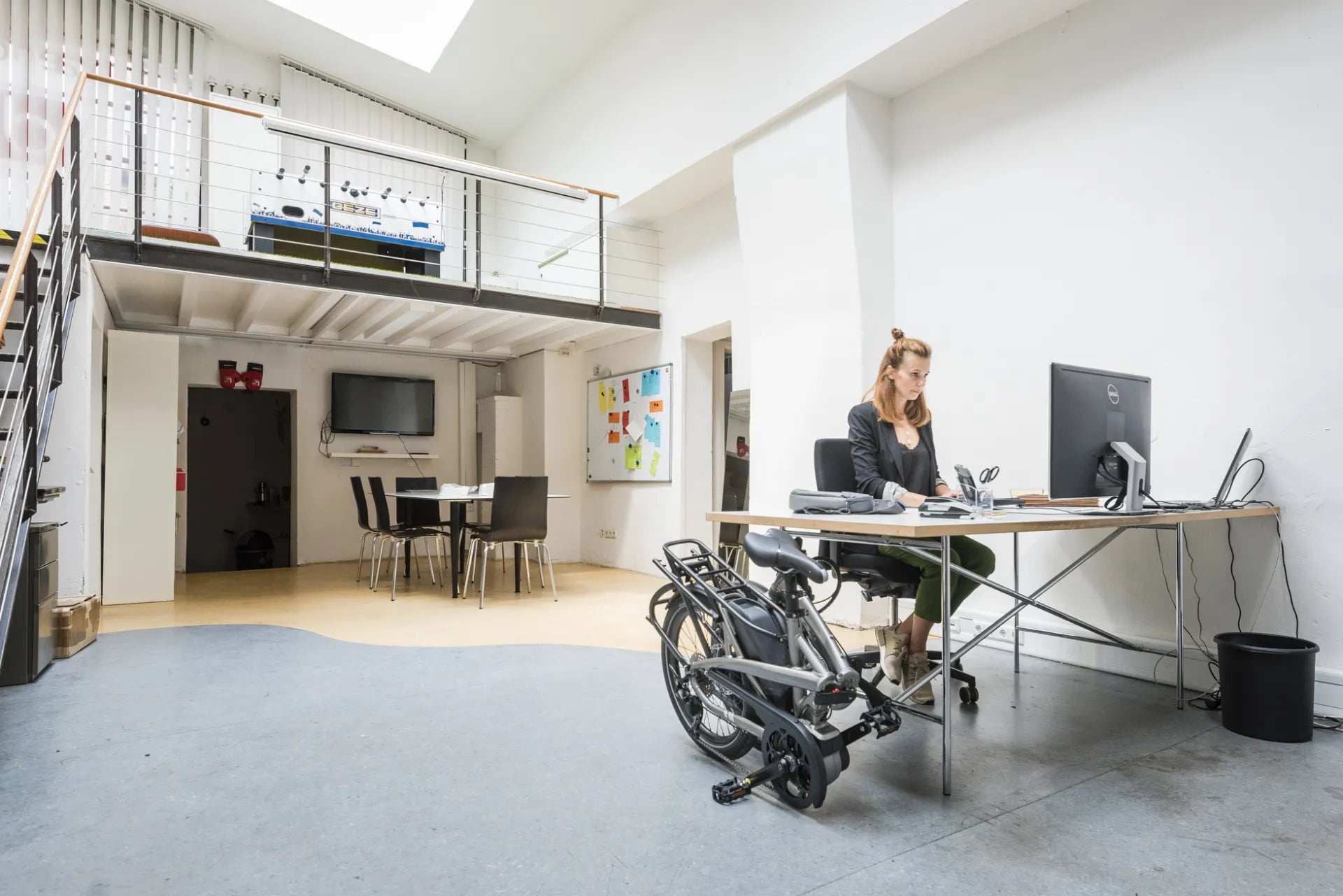 Woman in a loft office with a folding bike next to a desk.