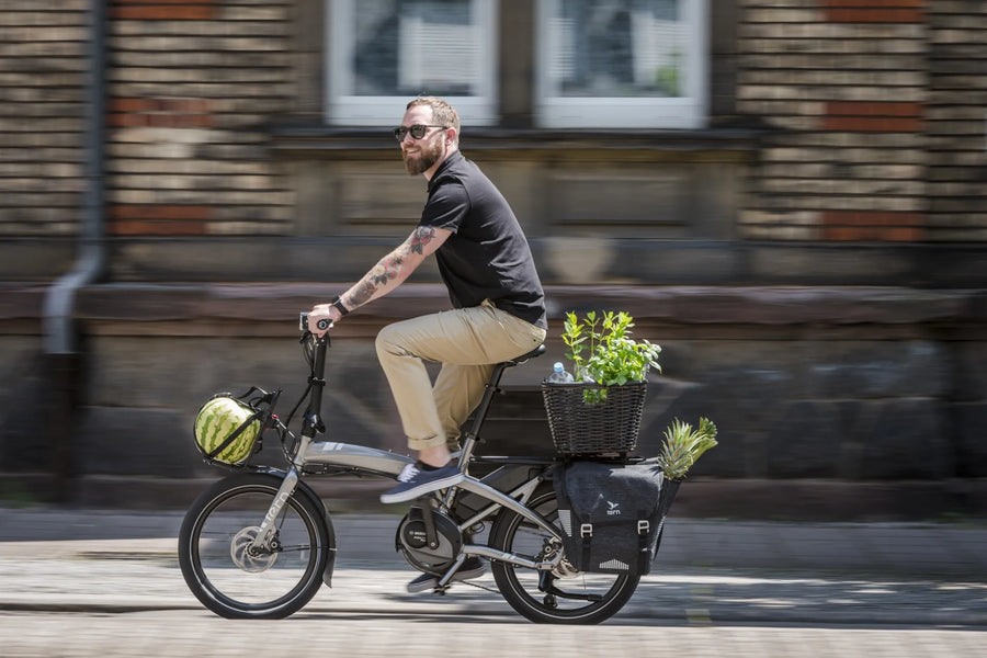 Man riding a cargo bike with plants in an urban setting