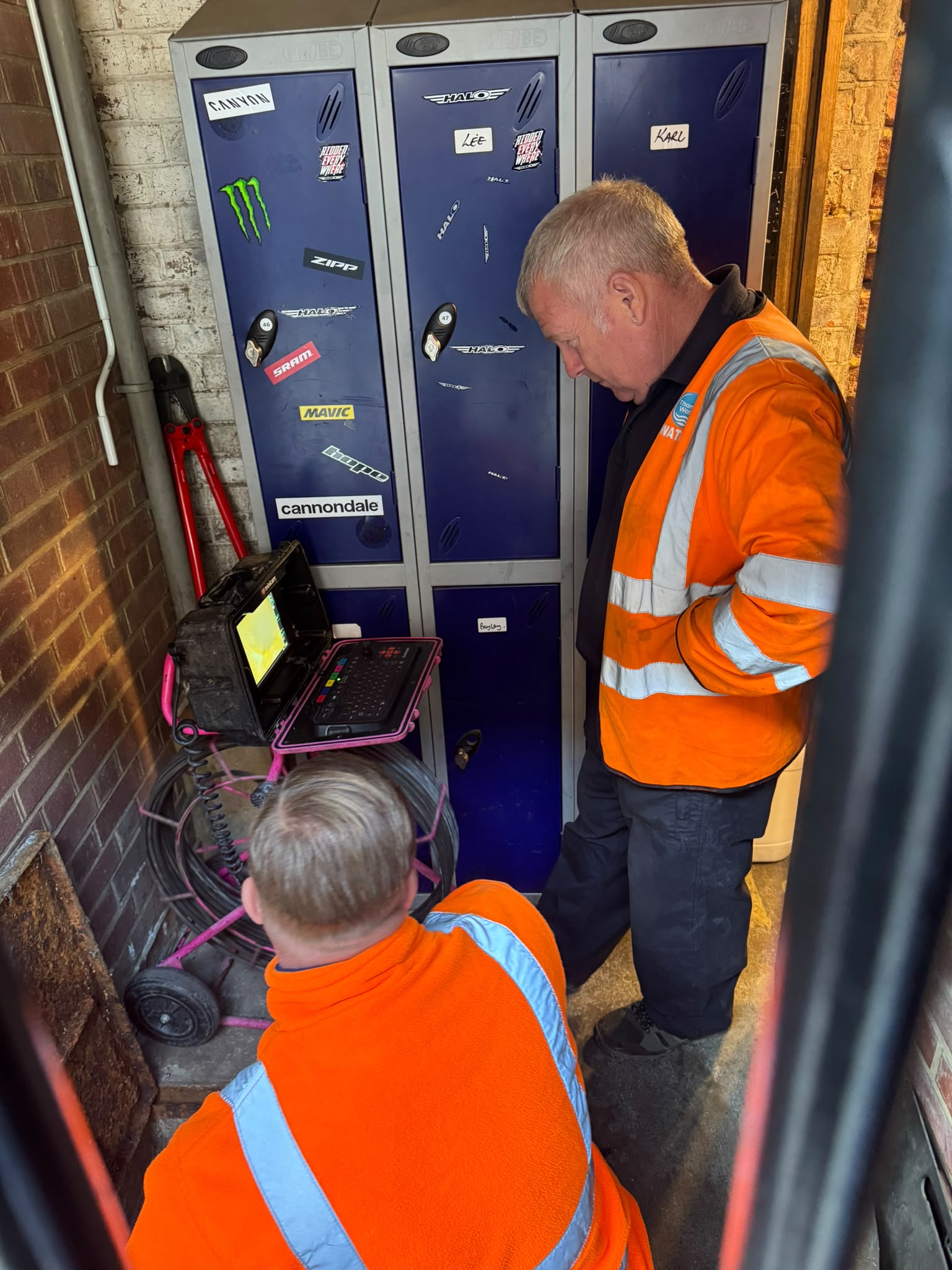 Two workers in orange high-visibility clothing using inspection equipment beside the lockers at our Herne Hill workshop.
